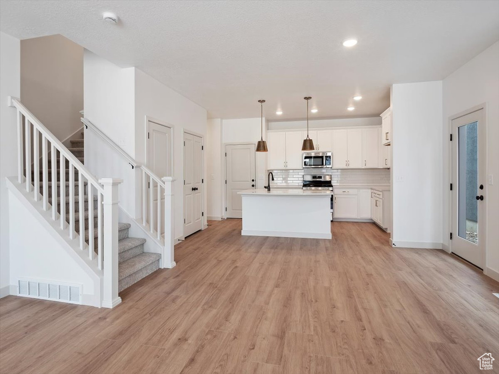 Kitchen with light wood-type flooring, pendant lighting, sink, stainless steel appliances, and white cabinetry