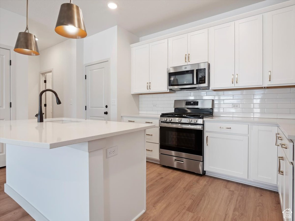 Kitchen featuring white cabinetry, decorative light fixtures, appliances with stainless steel finishes, and a kitchen island with sink