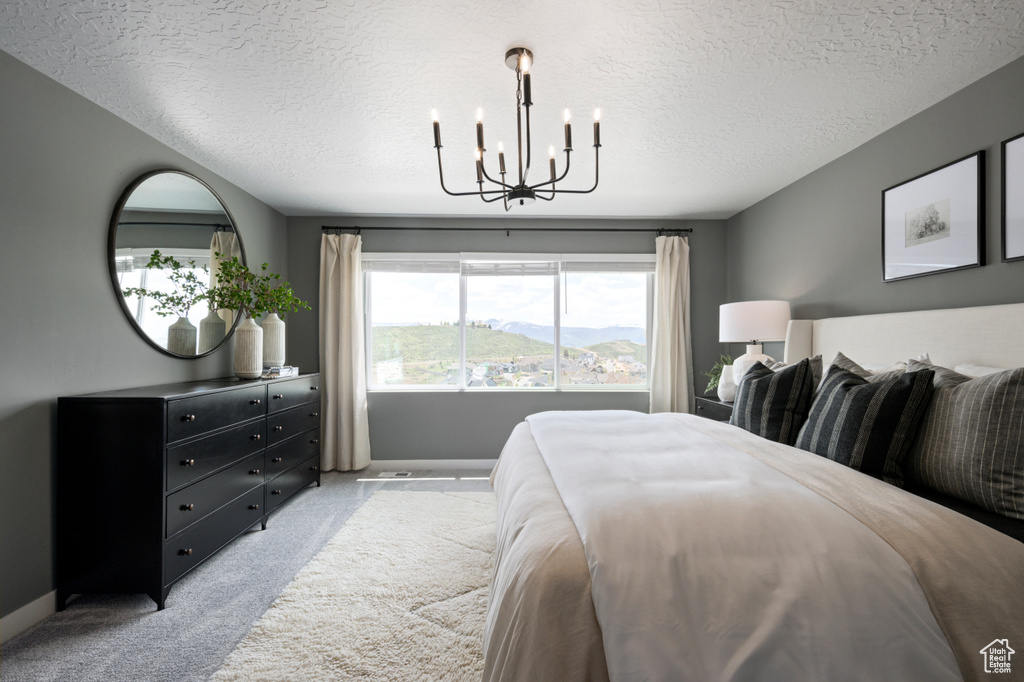 Bedroom with a mountain view, a textured ceiling, light colored carpet, and a notable chandelier