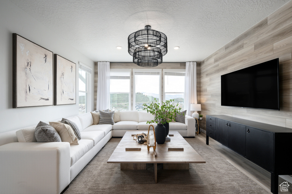 Living room with wood walls, wood-type flooring, an inviting chandelier, and a textured ceiling