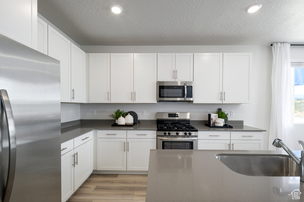 Kitchen featuring light hardwood / wood-style flooring, sink, white cabinets, appliances with stainless steel finishes, and a textured ceiling