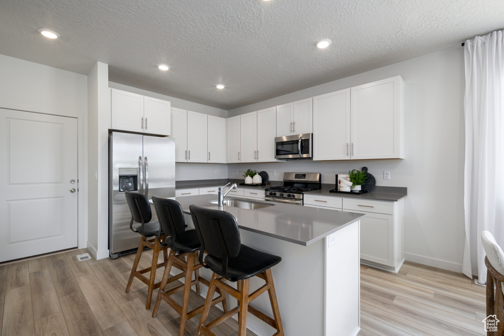 Kitchen with appliances with stainless steel finishes, a center island with sink, and white cabinets