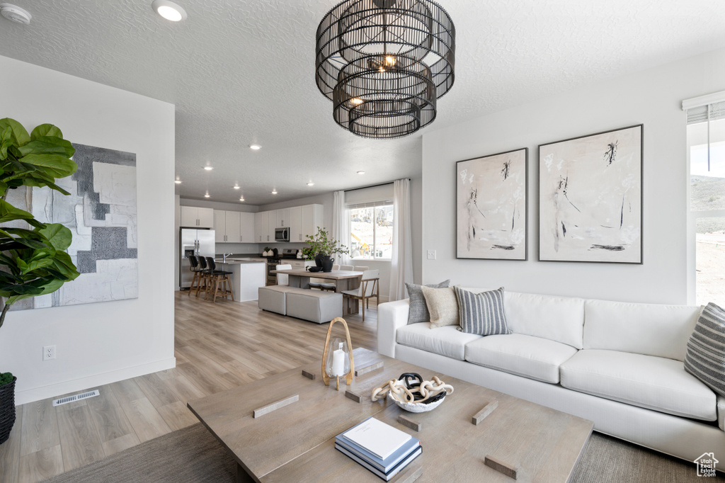 Living room featuring an inviting chandelier, light hardwood / wood-style floors, and a textured ceiling