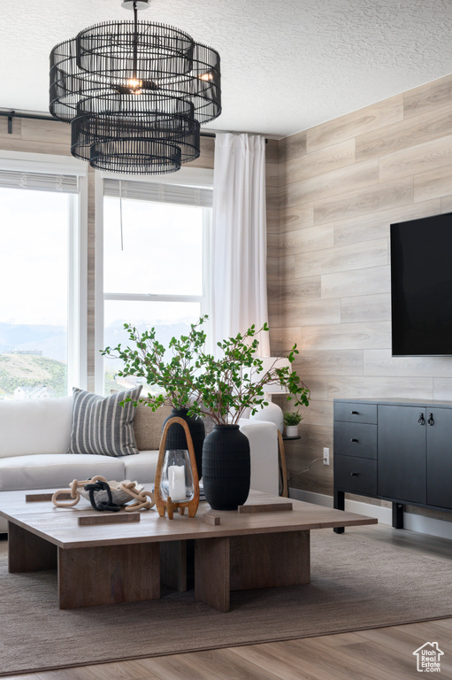 Living room with wood walls, wood-type flooring, a notable chandelier, and a textured ceiling