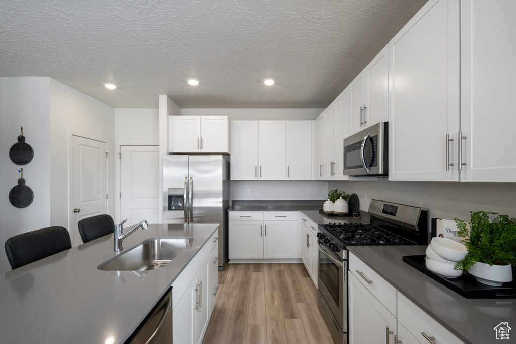 Kitchen featuring light hardwood / wood-style floors, sink, white cabinets, appliances with stainless steel finishes, and a textured ceiling