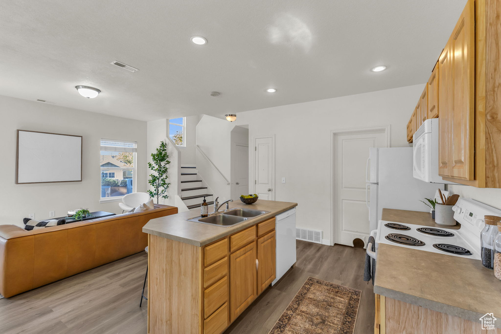 Kitchen featuring an island with sink, sink, white appliances, wood-type flooring, and light brown cabinetry