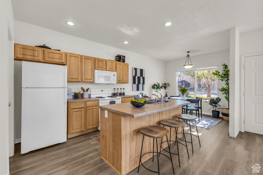 Kitchen featuring light wood-type flooring, white appliances, decorative light fixtures, a center island with sink, and sink