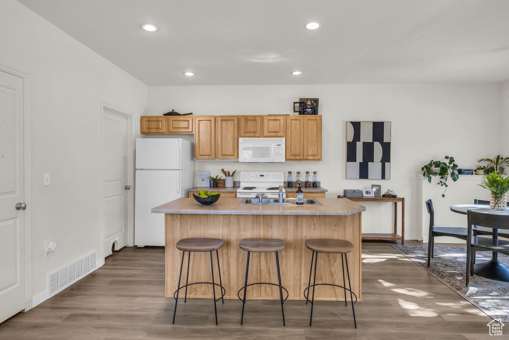 Kitchen featuring a kitchen breakfast bar, white appliances, a kitchen island with sink, and dark hardwood / wood-style floors