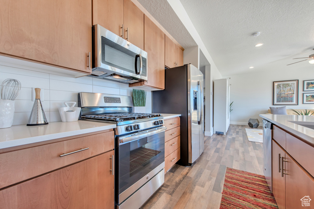 Kitchen featuring ceiling fan, a textured ceiling, appliances with stainless steel finishes, light hardwood / wood-style floors, and decorative backsplash