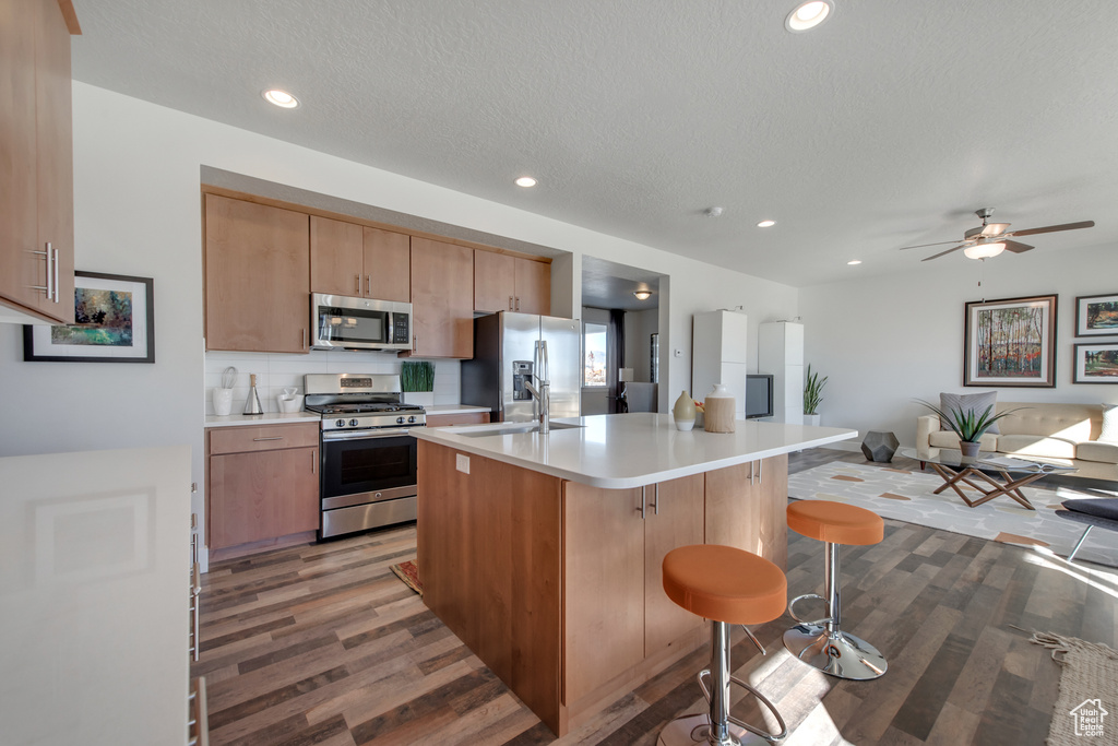 Kitchen with a kitchen island with sink, wood-type flooring, stainless steel appliances, a kitchen bar, and a textured ceiling