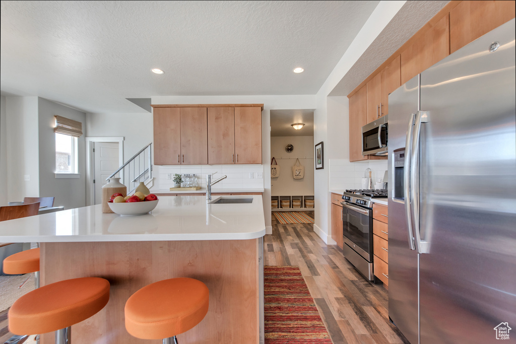 Kitchen with sink, wood-type flooring, a center island with sink, backsplash, and stainless steel appliances