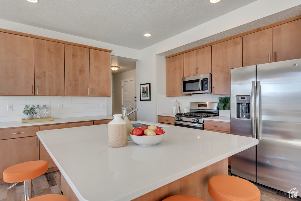 Kitchen featuring backsplash, appliances with stainless steel finishes, a center island, and a kitchen breakfast bar