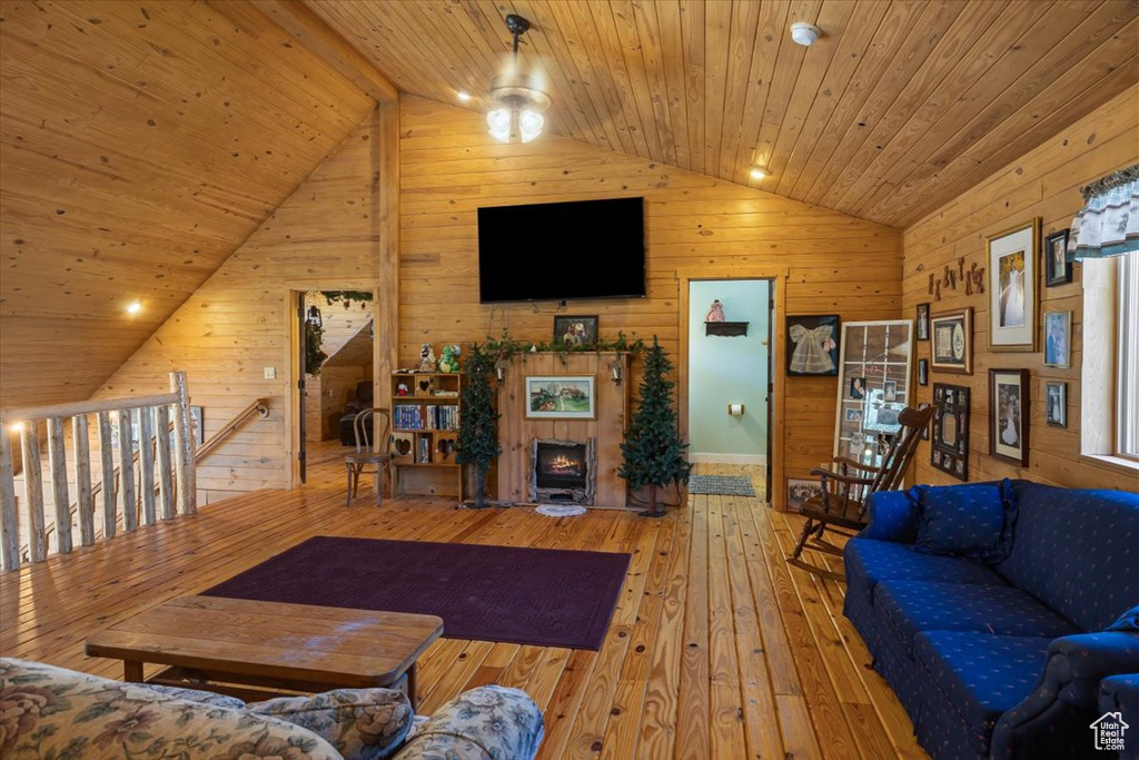 Living room featuring lofted ceiling, wooden walls, ceiling fan, wood ceiling, and light hardwood / wood-style floors