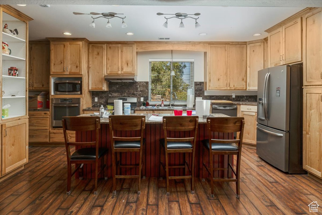 Kitchen featuring a kitchen island, dark hardwood / wood-style flooring, a kitchen breakfast bar, light stone countertops, and appliances with stainless steel finishes