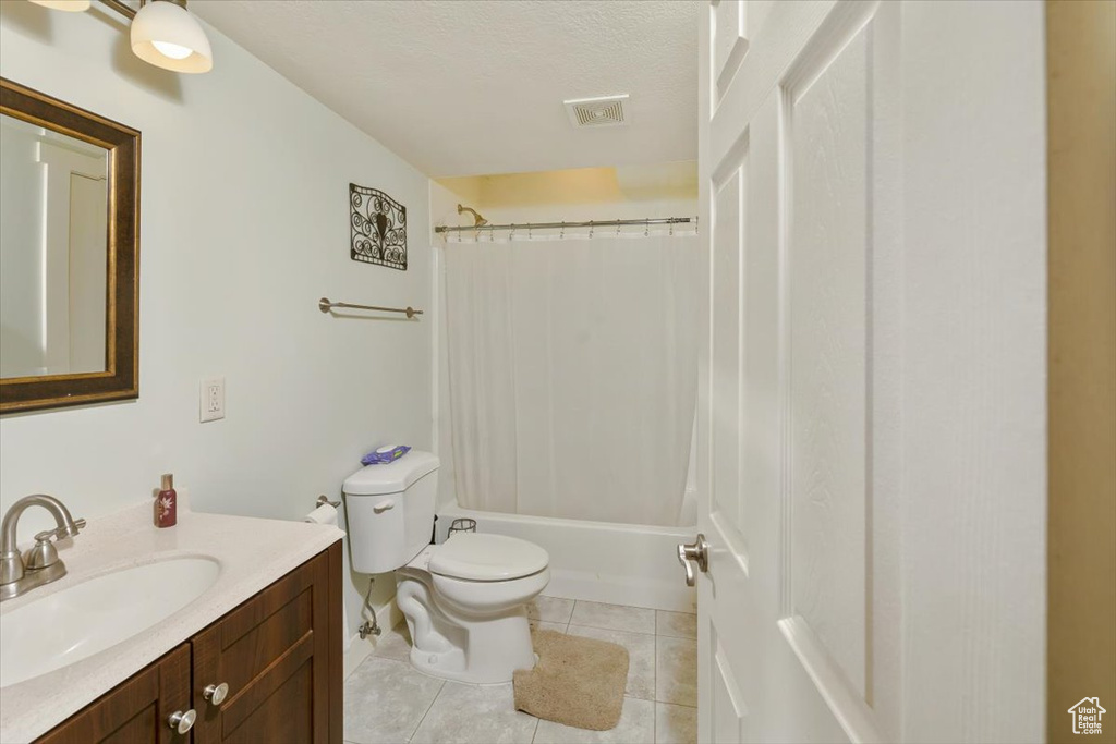 Full bathroom featuring vanity, shower / bath combination with curtain, tile patterned flooring, toilet, and a textured ceiling