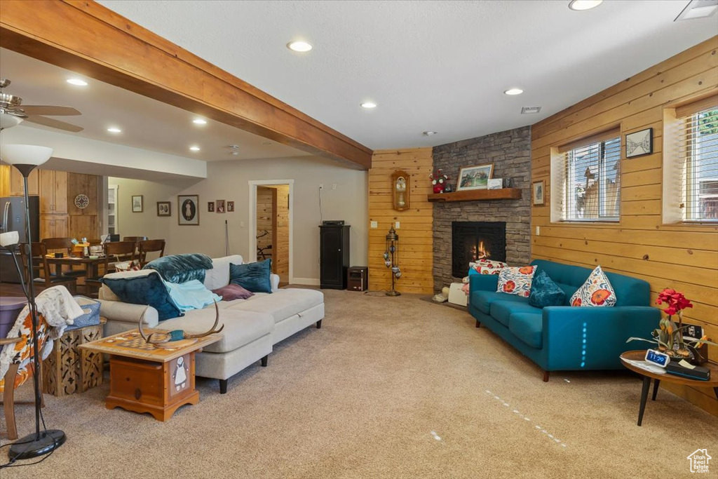 Carpeted living room with ceiling fan, a stone fireplace, beamed ceiling, and wooden walls