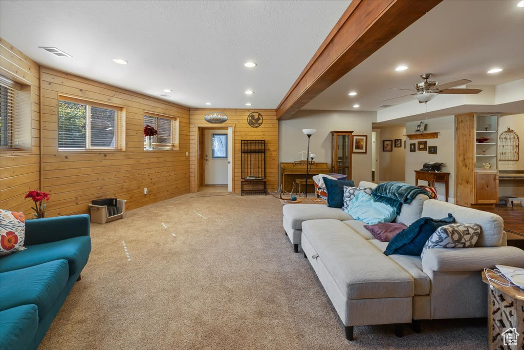 Carpeted living room featuring ceiling fan, wood walls, and beam ceiling