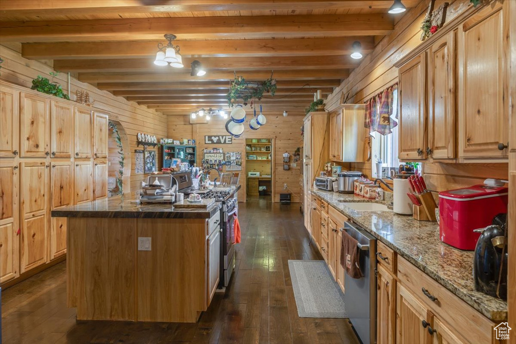 Kitchen featuring beamed ceiling, stainless steel appliances, wood walls, and a center island