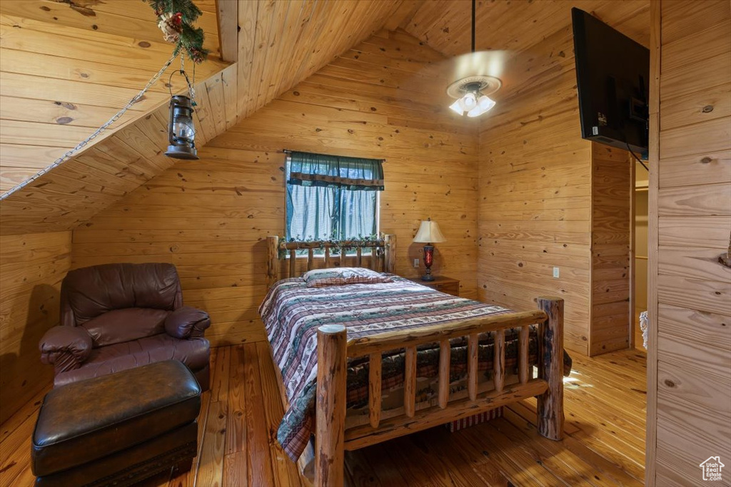 Bedroom featuring wooden walls, vaulted ceiling, and wood-type flooring