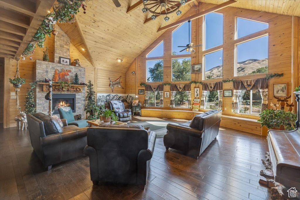 Living room with high vaulted ceiling, wooden walls, dark wood-type flooring, a fireplace, and beam ceiling