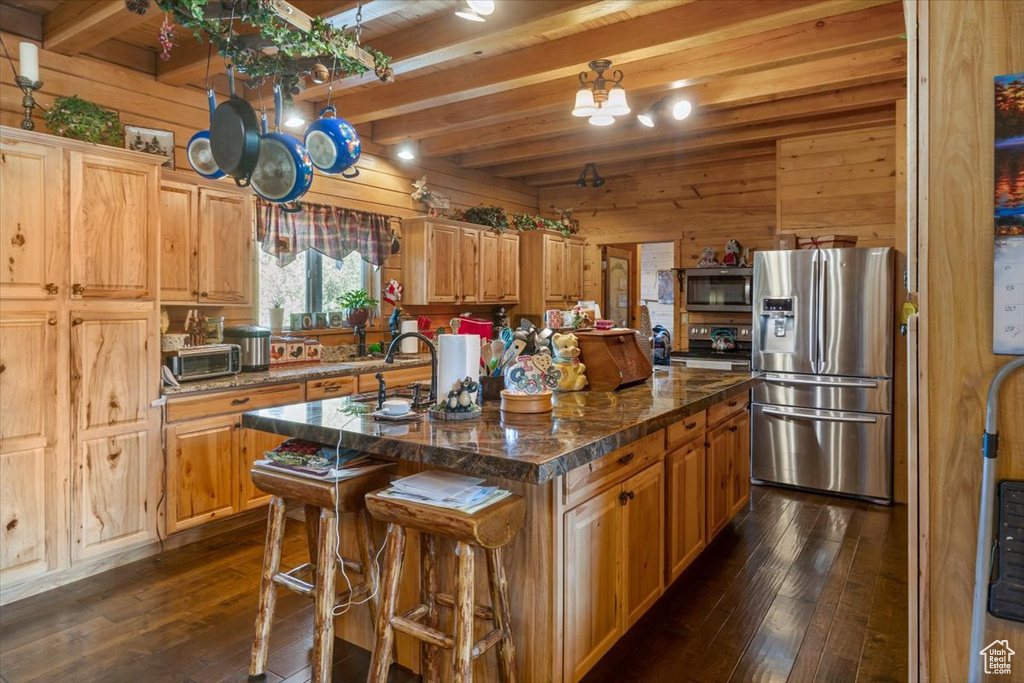 Kitchen featuring beamed ceiling, wooden walls, stainless steel appliances, dark hardwood / wood-style floors, and a center island