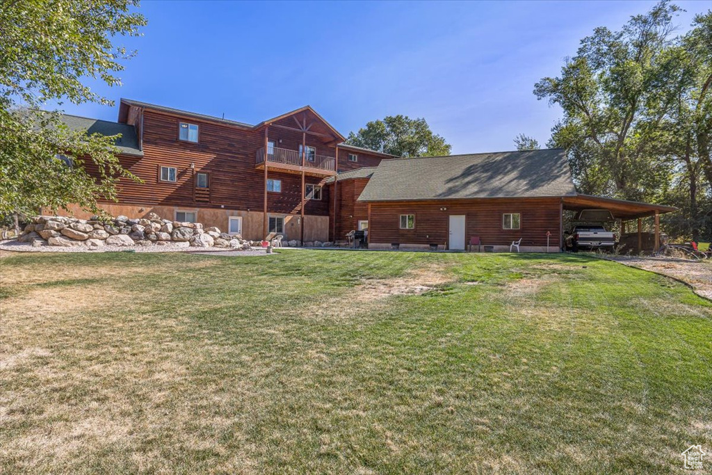 Back of house with a carport, a balcony, and a lawn