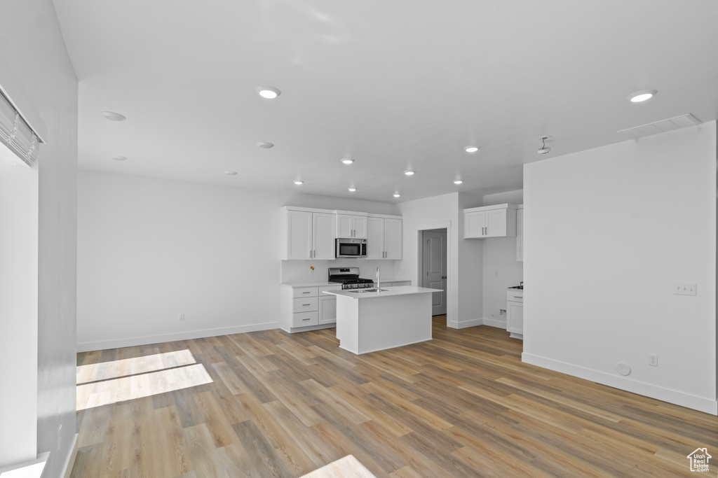 Kitchen with appliances with stainless steel finishes, a center island with sink, light hardwood / wood-style flooring, and white cabinetry