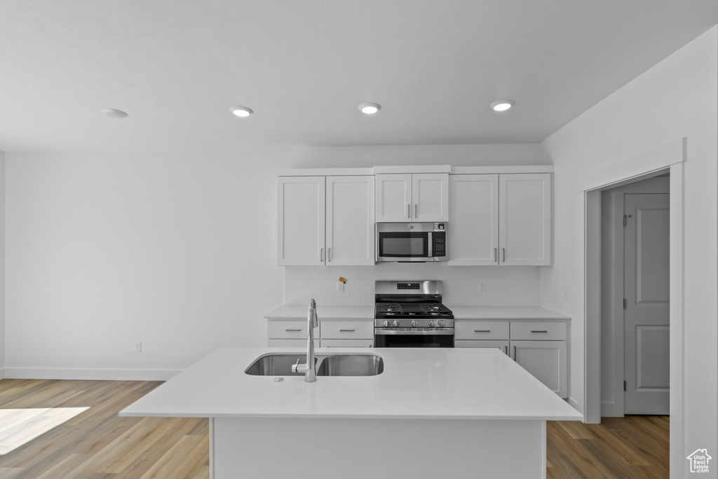 Kitchen with light wood-type flooring, sink, stainless steel appliances, an island with sink, and white cabinetry