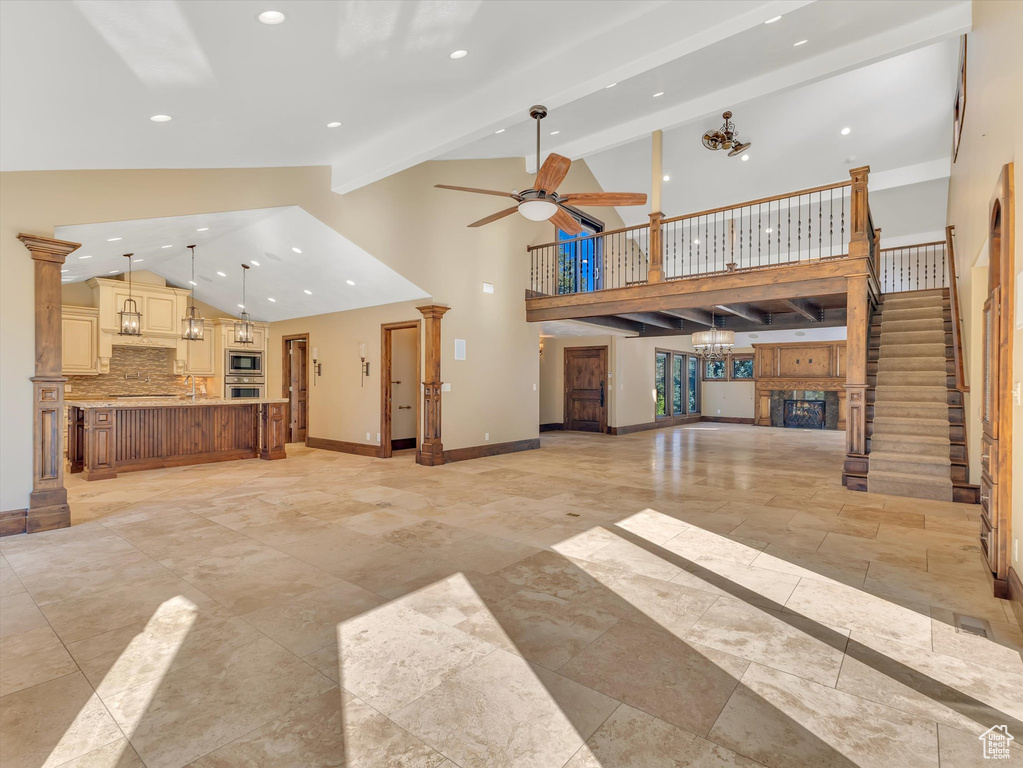 Unfurnished living room featuring ornate columns, high vaulted ceiling, ceiling fan, and beamed ceiling