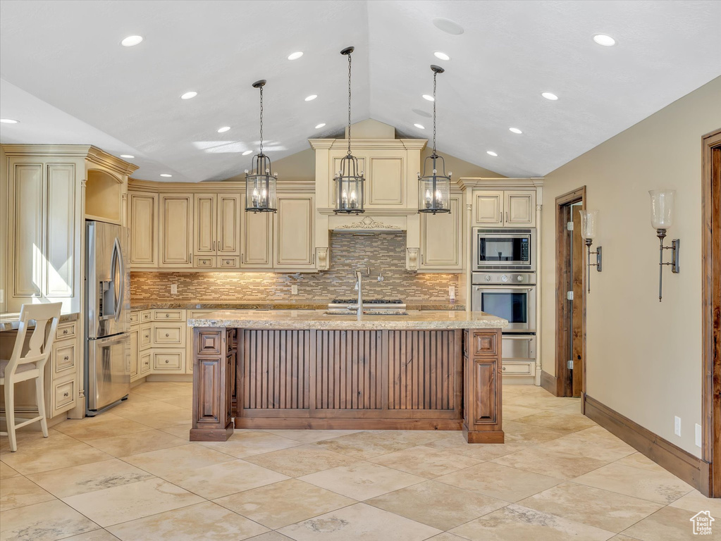 Kitchen featuring light stone counters, a center island with sink, stainless steel appliances, and hanging light fixtures