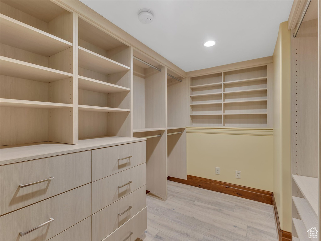 Walk in closet with light hardwood / wood-style flooring