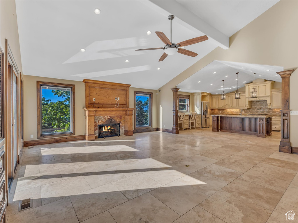 Unfurnished living room with high vaulted ceiling, beamed ceiling, ceiling fan, ornate columns, and a large fireplace