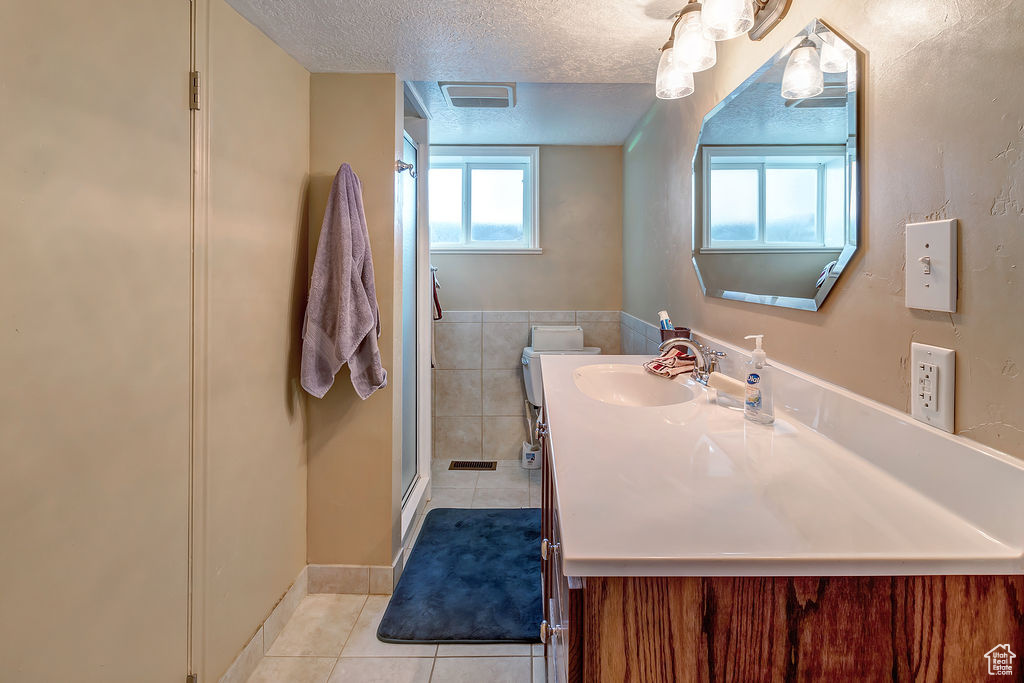 Bathroom featuring vanity, a textured ceiling, tile patterned floors, tile walls, and a shower with door