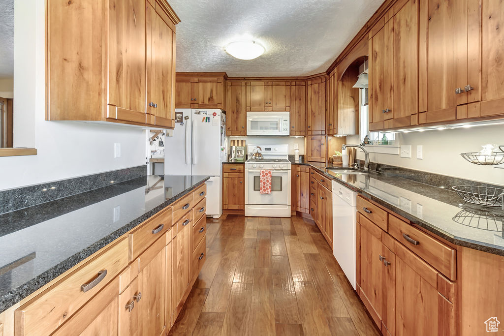 Kitchen with hardwood / wood-style floors, dark stone countertops, white appliances, sink, and a textured ceiling