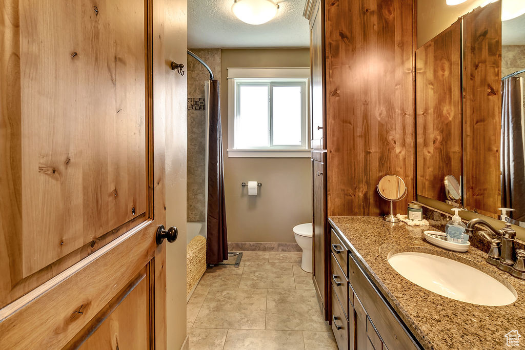 Full bathroom featuring shower / bath combination with curtain, vanity, toilet, a textured ceiling, and tile patterned flooring