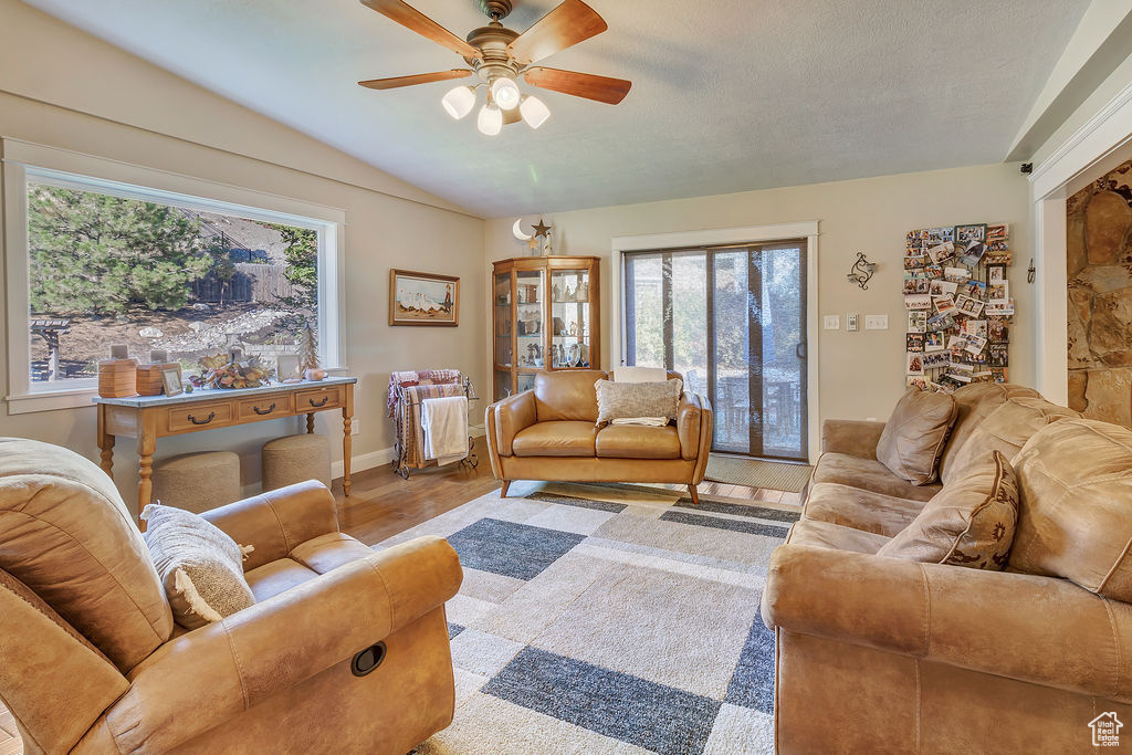 Living room featuring a textured ceiling, vaulted ceiling, light wood-type flooring, and ceiling fan