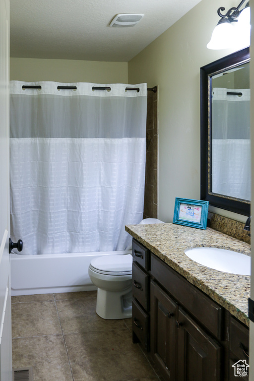 Full bathroom featuring toilet, tile patterned floors, shower / bath combination with curtain, vanity, and a textured ceiling