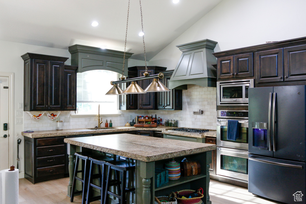 Kitchen with lofted ceiling, tasteful backsplash, a kitchen island, stainless steel appliances, and light wood-type flooring