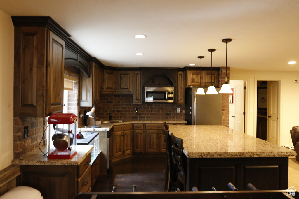 Kitchen with a kitchen island, light stone counters, dark hardwood / wood-style floors, sink, and backsplash