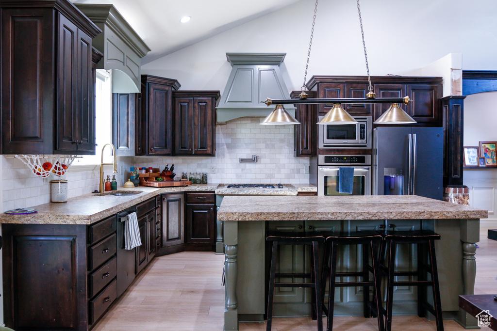 Kitchen with lofted ceiling, sink, a kitchen island, appliances with stainless steel finishes, and a breakfast bar area