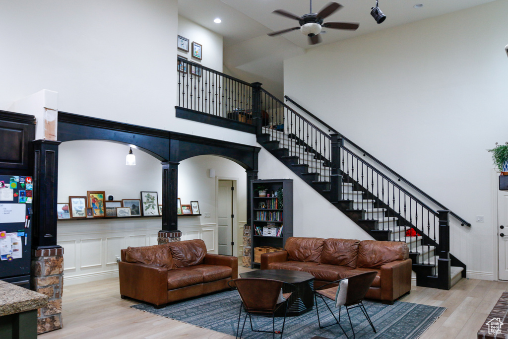 Living room featuring ornate columns, a towering ceiling, light wood-type flooring, and ceiling fan