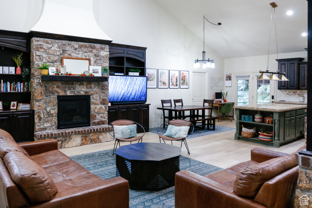 Living room featuring a fireplace, light hardwood / wood-style floors, high vaulted ceiling, and a notable chandelier