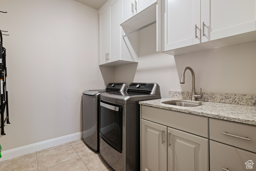 Laundry area featuring light tile patterned flooring, washer and clothes dryer, sink, and cabinets