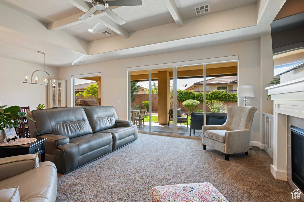 Carpeted living room with a fireplace, ceiling fan with notable chandelier, and beam ceiling