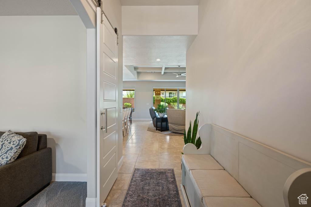 Hall featuring light tile patterned flooring, beam ceiling, and a barn door