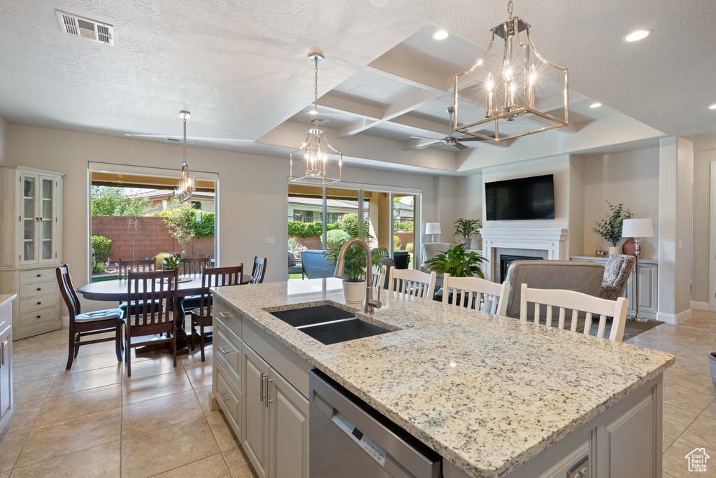 Kitchen with an island with sink, light stone countertops, sink, coffered ceiling, and dishwasher