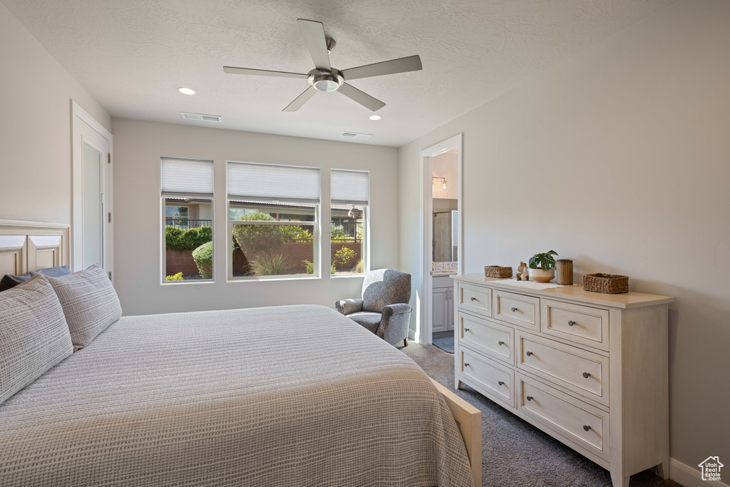 Bedroom featuring ceiling fan, a textured ceiling, ensuite bathroom, and dark carpet