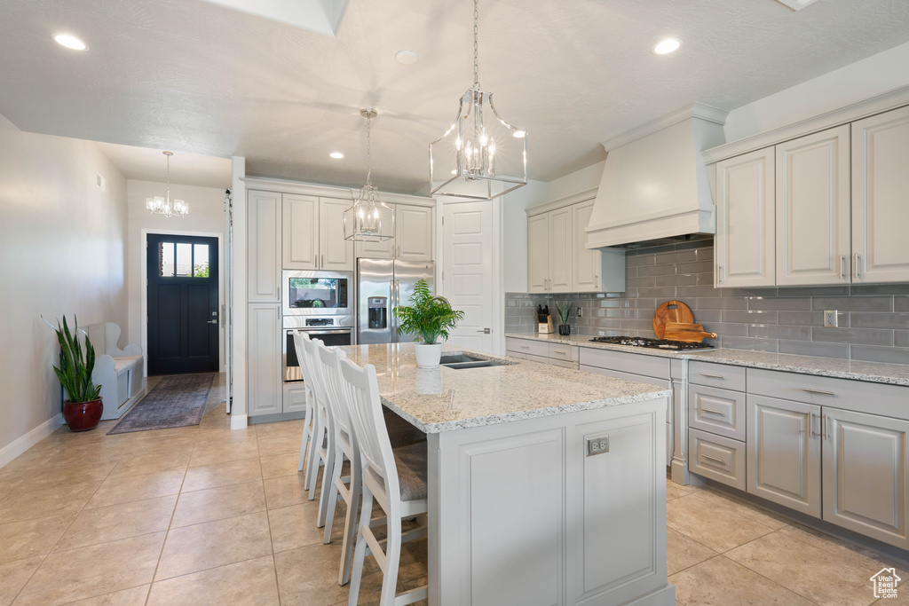 Kitchen with pendant lighting, premium range hood, stainless steel appliances, a center island, and light stone countertops