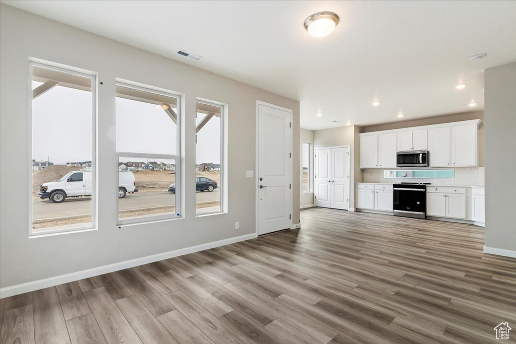 Kitchen with light wood-type flooring, appliances with stainless steel finishes, a wealth of natural light, and white cabinetry