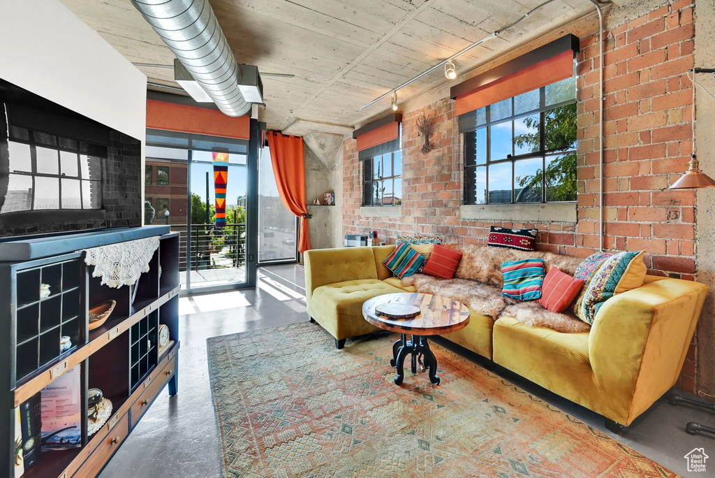 Living room with track lighting, a healthy amount of sunlight, brick wall, and concrete floors